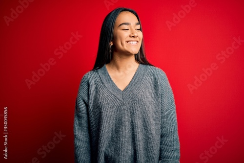Young beautiful asian woman wearing casual sweater standing over isolated red background looking away to side with smile on face, natural expression. Laughing confident. © Krakenimages.com