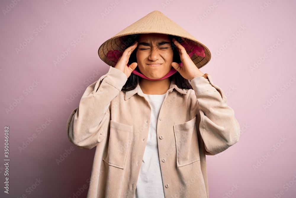 Young beautiful woman wearing traditional conical asian hat over isolated pink background suffering from headache desperate and stressed because pain and migraine. Hands on head. Young beautiful woman wearing traditional conical asian hat over isolated pink background suffering from headache desperate and stressed because pain and migraine. Hands on head.