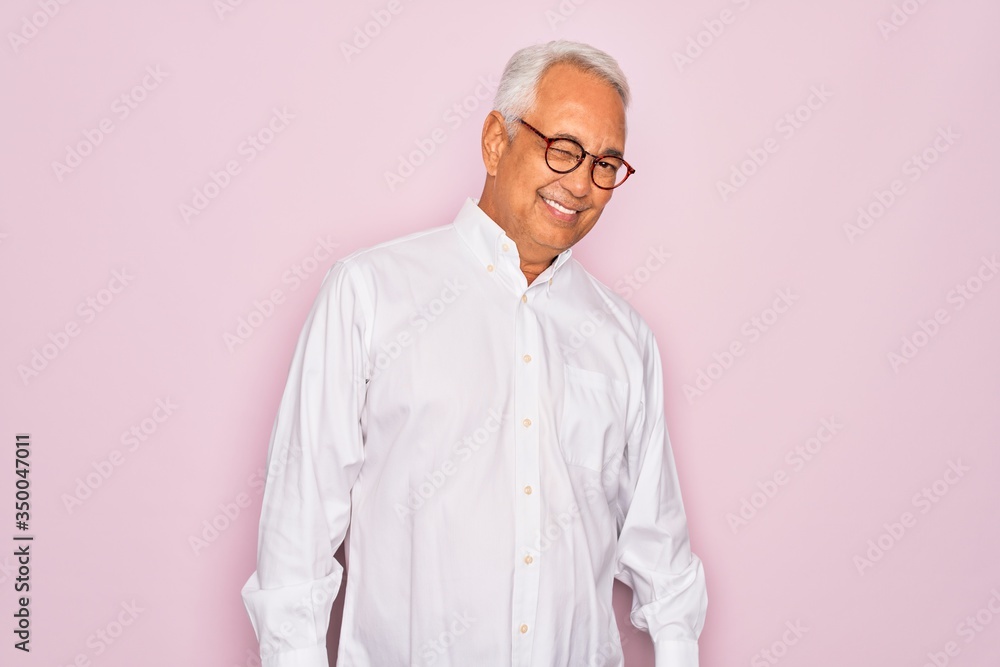 Middle age senior grey-haired man wearing glasses and business shirt over pink background winking looking at the camera with sexy expression, cheerful and happy face. Middle age senior grey-haired man wearing glasses and business shirt over pink background winking looking at the camera with sexy expression, cheerful and happy face.