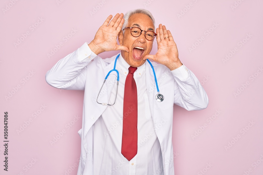 Middle age senior grey-haired doctor man wearing stethoscope and professional medical coat Smiling cheerful playing peek a boo with hands showing face. Surprised and exited
