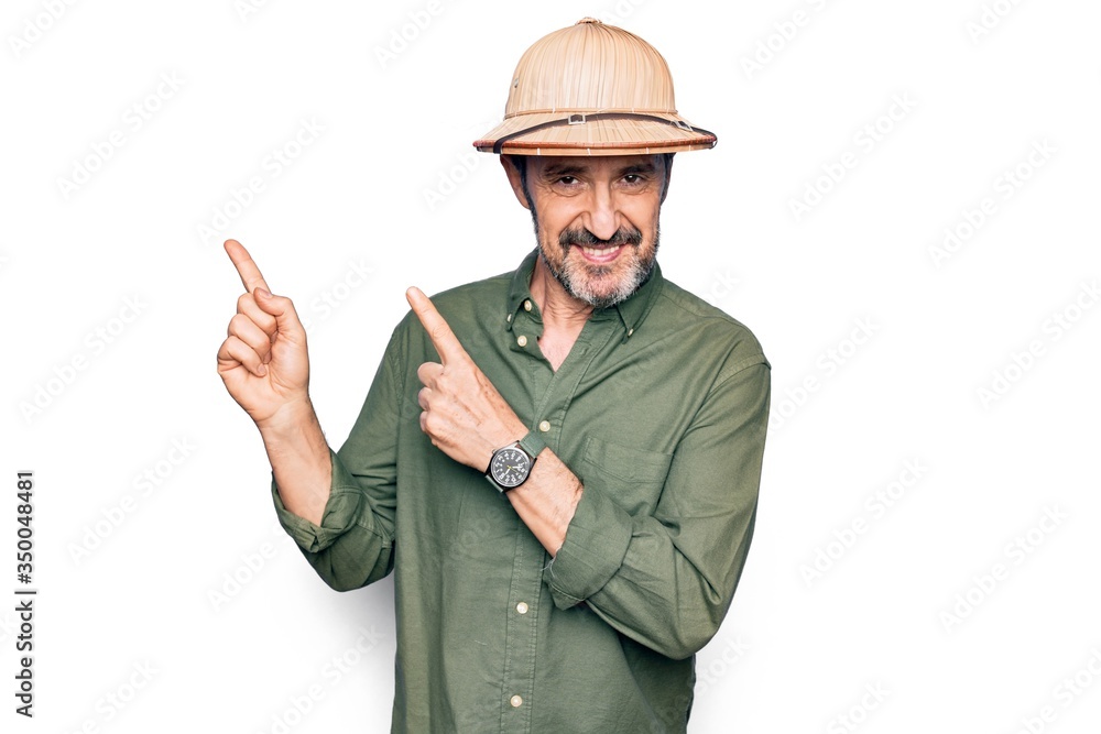 Middle age tourist man on vacation wearing explorer hat over isolated white background smiling and looking at the camera pointing with two hands and fingers to the side. Middle age tourist man on vacation wearing explorer hat over isolated white background smiling and looking at the camera pointing with two hands and fingers to the side.
