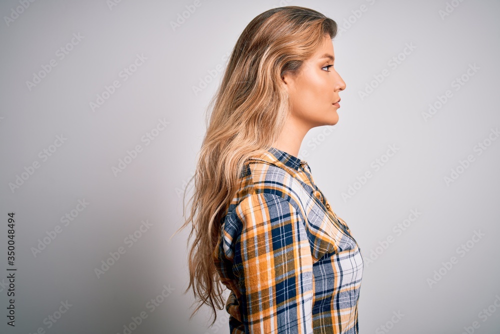Young beautiful blonde woman wearing casual shirt standing over isolated white background looking to side, relax profile pose with natural face with confident smile. Young beautiful blonde woman wearing casual shirt standing over isolated white background looking to side, relax profile pose with natural face with confident smile.