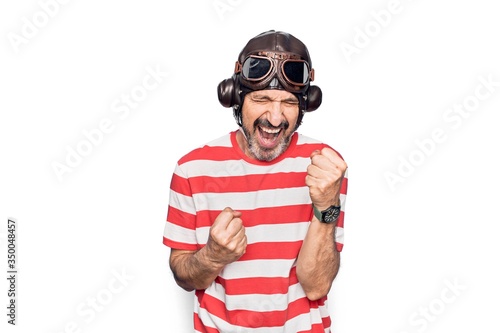 Middle age aviator man wearing vintage helmet and glasses over isolated white background celebrating surprised and amazed for success with arms raised and eyes closed © Krakenimages.com