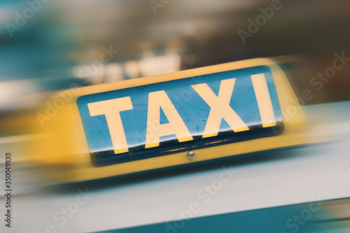 Yellow taxi sign on top of taxi cab. Fast public transport service car on city background. Motion blur, selective focus