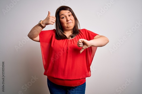 Beautiful brunette plus size woman wearing casual red t-shirt over isolated white background Doing thumbs up and down, disagreement and agreement expression. Crazy conflict