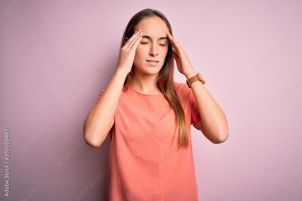 Young beautiful woman wearing casual t-shirt standing over isolated pink background with hand on head for pain in head because stress. Suffering migraine. Young beautiful woman wearing casual t-shirt standing over isolated pink background with hand on head for pain in head because stress. Suffering migraine.