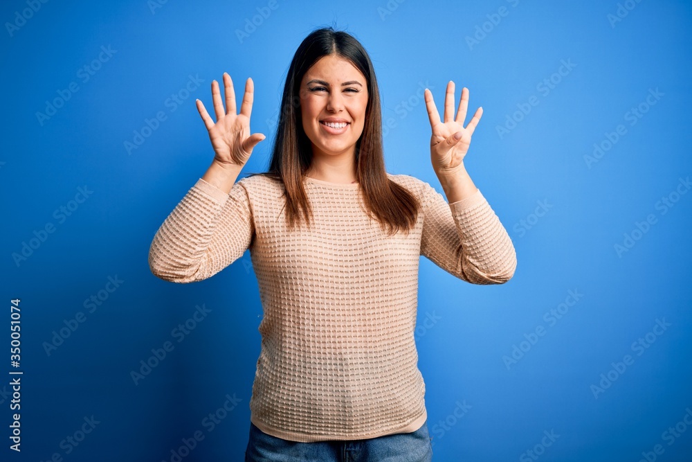Young beautiful woman wearing casual sweater over blue background showing and pointing up with fingers number nine while smiling confident and happy. Young beautiful woman wearing casual sweater over blue background showing and pointing up with fingers number nine while smiling confident and happy.