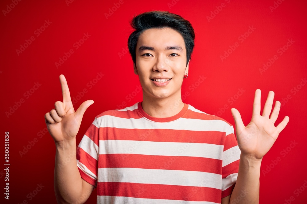 Young handsome chinese man wearing casual striped t-shirt standing over red background showing and pointing up with fingers number seven while smiling confident and happy. Young handsome chinese man wearing casual striped t-shirt standing over red background showing and pointing up with fingers number seven while smiling confident and happy.