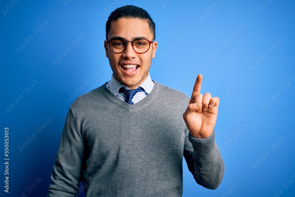 Young brazilian businessman wearing tie standing over isolated blue background pointing finger up with successful idea. Exited and happy. Number one. Young brazilian businessman wearing tie standing over isolated blue background pointing finger up with successful idea. Exited and happy. Number one.