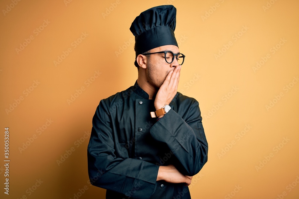 Young brazilian chef man wearing cooker uniform and hat over isolated yellow background bored yawning tired covering mouth with hand. Restless and sleepiness.