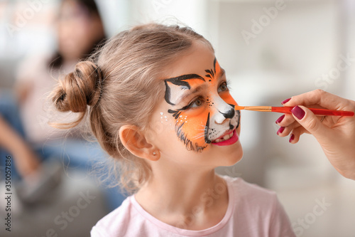 Woman painting face of little girl at home