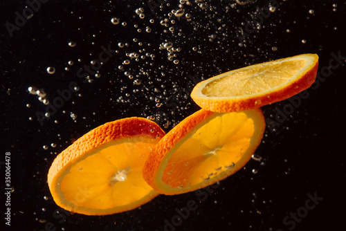 Three orange slices splash in water on black background