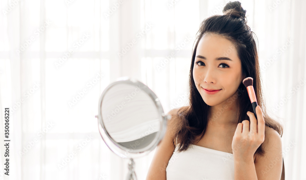 Smiling of young beautiful pretty asian woman clean fresh healthy white skin looking at mirror.girl touching on her face with hand and applying cream at home.spa and beauty concept Smiling of young beautiful pretty asian woman clean fresh healthy white skin looking at mirror.girl touching on her face with hand and applying cream at home.spa and beauty concept