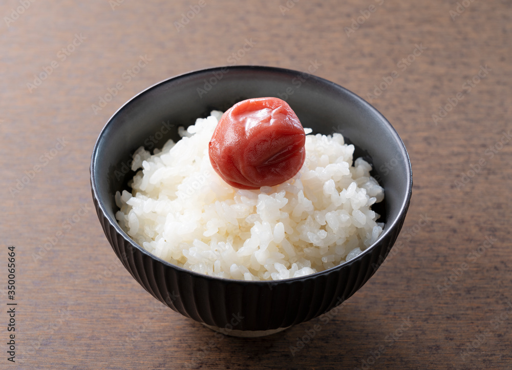 Japanese pickled plums and freshly cooked rice set against a wooden backdrop Japanese pickled plums and freshly cooked rice set against a wooden backdrop