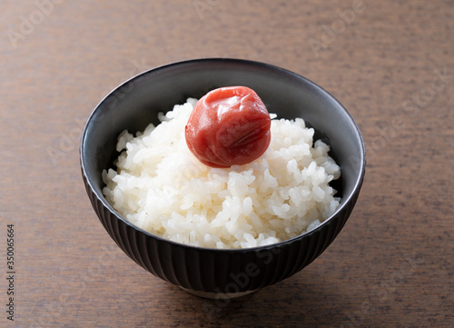 Japanese pickled plums and freshly cooked rice set against a wooden backdrop