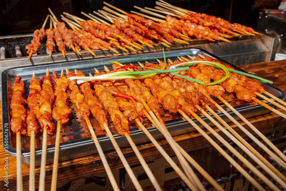 Street food. Chinese food. Juicy chicken skewers on skewers in a spicy sauce. With pepper and onion. Lie on a metal tray on a wooden table. Closeup shot.