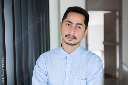 Young businessman asian smiling looking at camera. Portrait of a happy handsome young man in office. Close up face of young cool trendy man looking at camera.