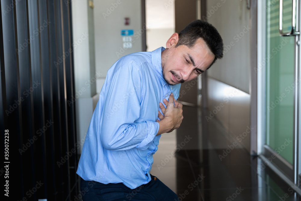 Young Businessman holding his heart in pain while in workplace.