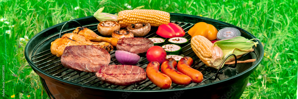 Barbecue panorama. Grilled meat, sausages, chicken, vegetables, with green grass in the background