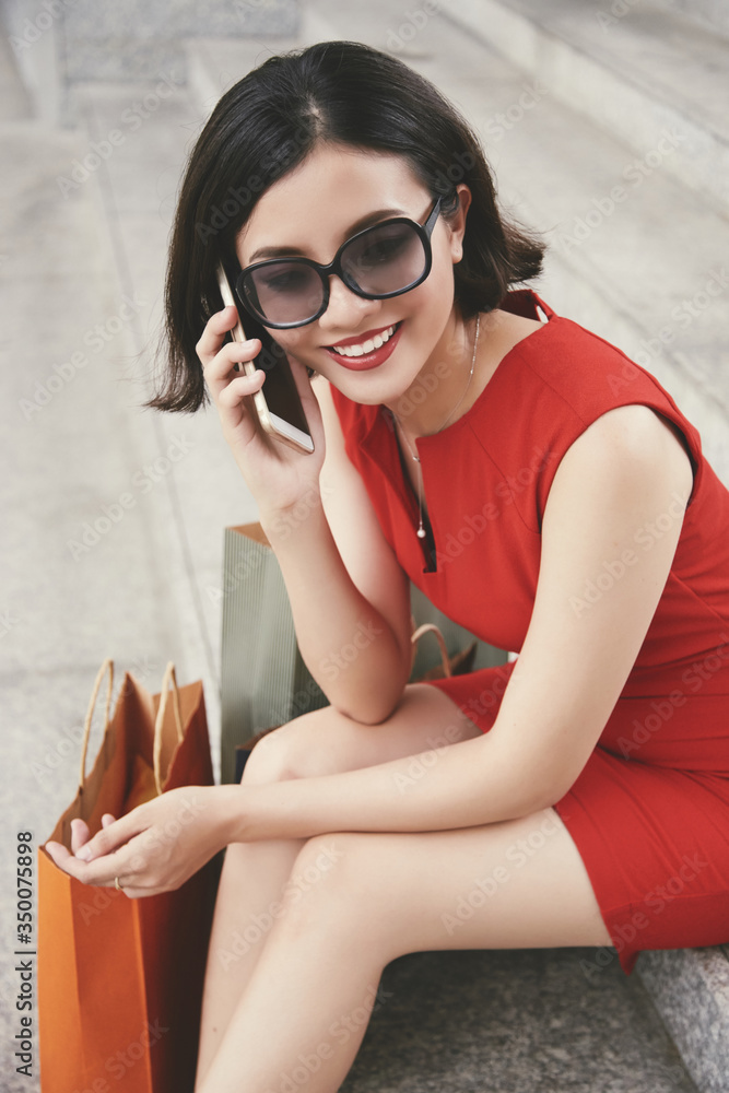 Beautiful elegant young woman in sunglasses sitting on steps and talking on phone with friend Beautiful elegant young woman in sunglasses sitting on steps and talking on phone with friend