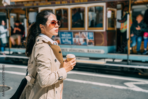 Photography Young woman standing on street drinking coffee to go while putting headphones on neck