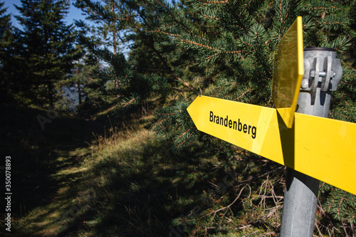 Yellow hiking signs on a pole pointing towards a hiking trail to Brandenberg, Austria in a pine forest. photo
