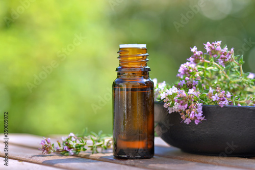 bottle of essential oil and flowers of aromatic herb on a table on green background