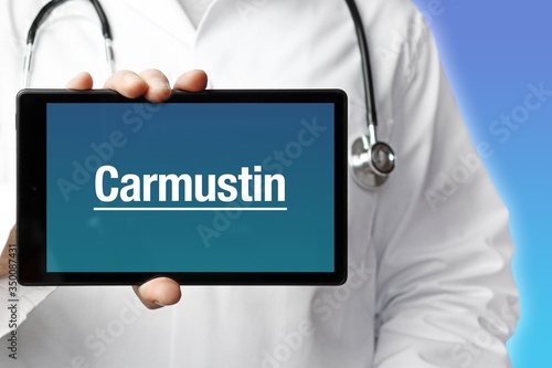 Carmustin. Arzt mit Stethoskop hält Tablet-Computer in Hand. Text im Display. Blauer Hintergrund. Krankheit, Gesundheit, Medizin photo