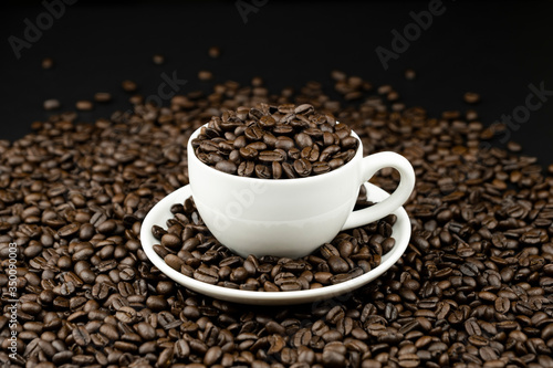 Roasted coffee beans in a white coffee cup on coffee beans field background