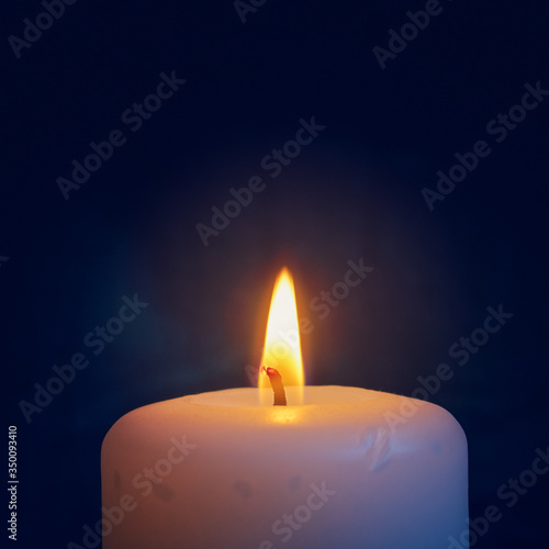 A burning white wax candle is on a dark background.