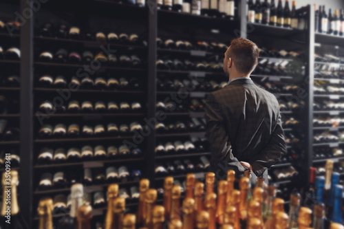 Sommelier Bartender choose wine bottle near rack store restaurant drinks