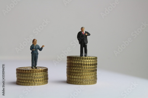 kleine Figuren auf unterschiedlich hohen Münzstapeln stehen für die ungleiche Bezahlung von Frauen und Männern
