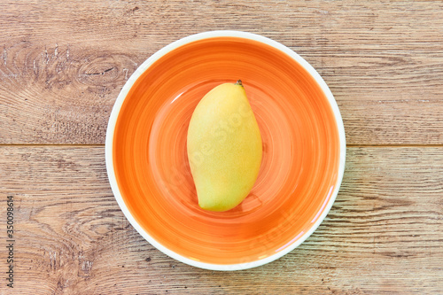 pale yellow mango on a orange plate on a wooden tabletop
