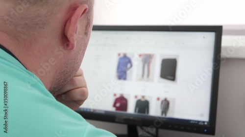 Shopping through a computer. A man looking and chooses wear in a clothing store to buy on the site. Browse a clothing to buy through a computer. Screen is blurred. Close Up.