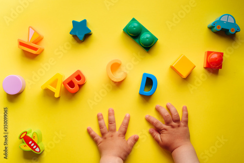 Child is playing with colorful constructor blocks. Kid's hands with bricks toy on yellow background. Educational toy, flat lay, top view.