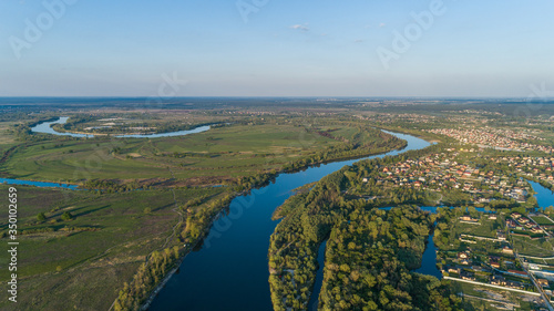Panoramic aerial view of the nature landscape with green meadows and a river at sunset.