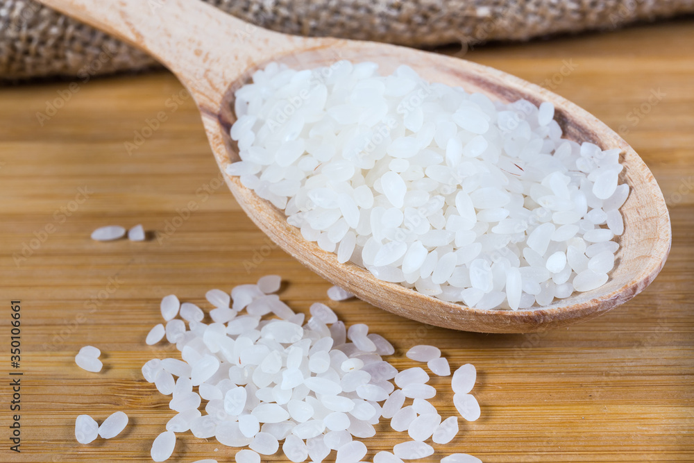 Uncooked camolino rice in wooden spoon on wooden surface closeup Uncooked camolino rice in wooden spoon on wooden surface closeup