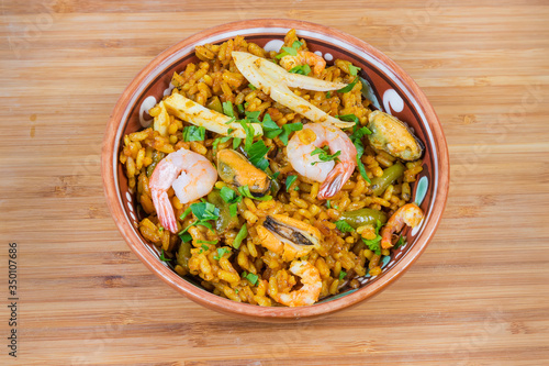 Cooked seafood paella in bowl on wooden surface