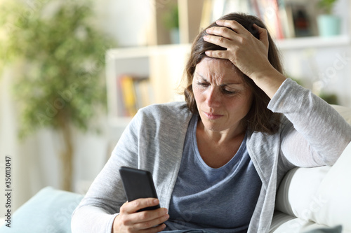 Sad adult woman reading news on phone at home