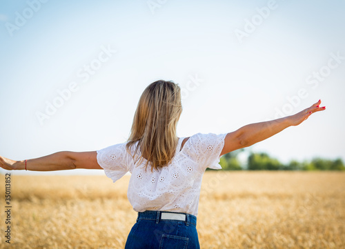 Blonde caucasian and happy girl in a white blouse and blue denim skirt in a wheat field enjoys freedom. Concept people in harmony with nature. Female psychology, feelings and emotions.