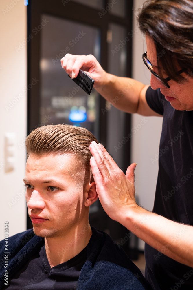 Fototapeta premium Barber combs the hair of a young man after cutting