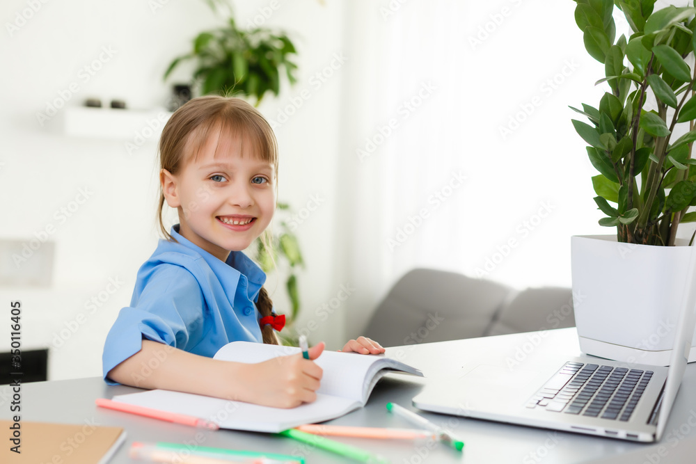 Cute little girl is sitting at table with her laptop and studying online Cute little girl is sitting at table with her laptop and studying online