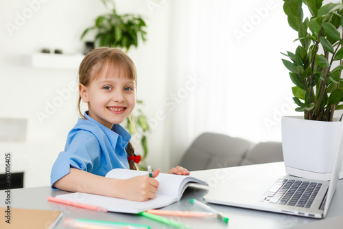 Cute little girl is sitting at table with her laptop and studying online