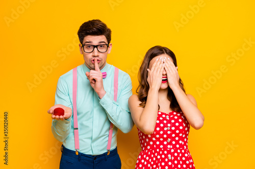 Photo of pretty lady closing eyes handsome guy boyfriend finger on lips hold girlfriend proposal ring box ask keep silence wear red dress shirt bowtie pants isolated yellow color background
