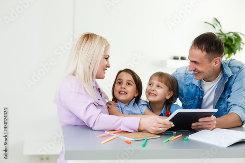 Happy family of four parents and cute little kids children enjoy using the tablet, watching cartoons, make internet video call or shopping online looking at computer screen sit together at home