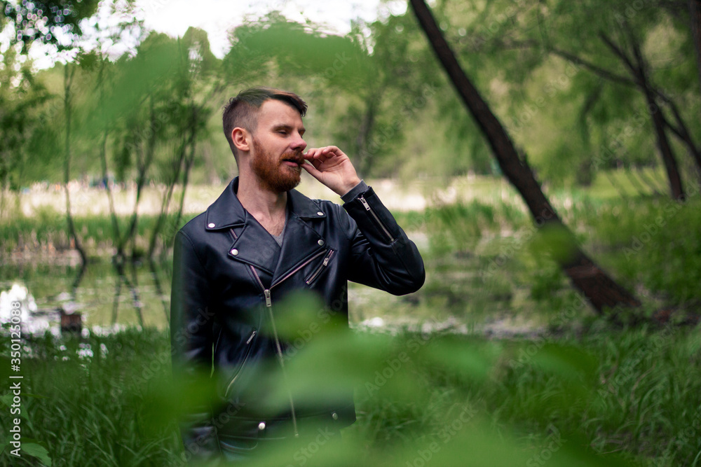 A guy with a red mustache and a beard trembles with a mustache against a green forest looking to the right. A guy with a red mustache and a beard trembles with a mustache against a green forest looking to the right.