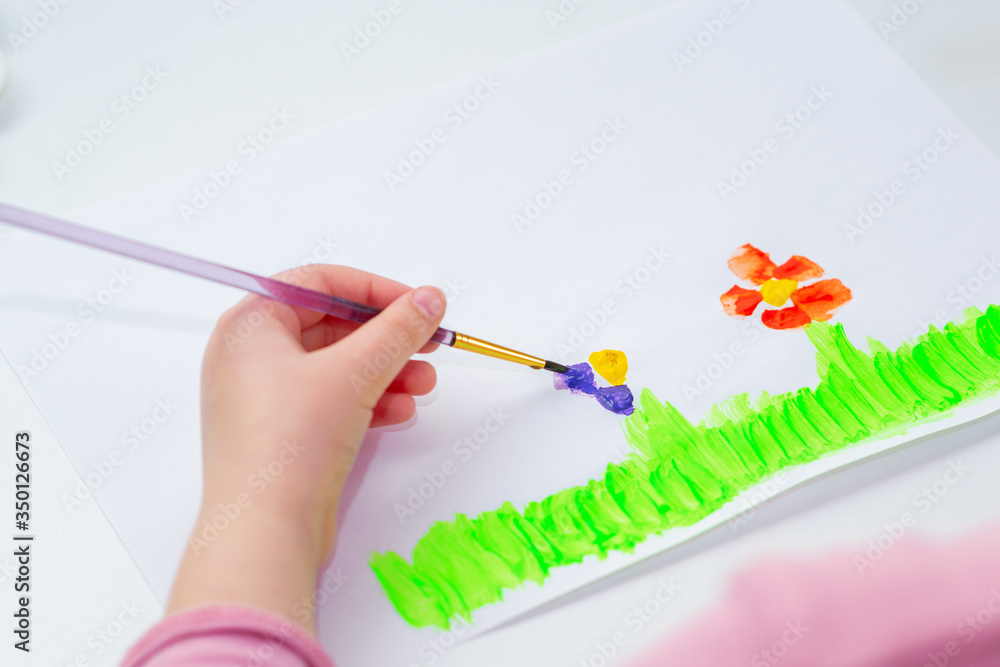 Child's left hand drawing flowers on white sheet of paper. Child's left hand drawing flowers on white sheet of paper.