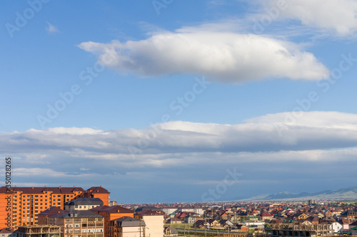 White clouds on the blue clean sky with sun rays above a city.  © mahovik