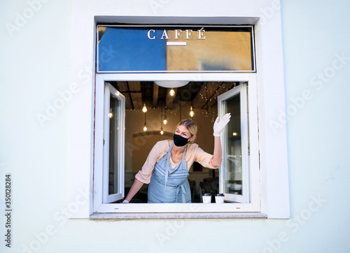 Woman with face mask serving coffee through window, shop open after lockdown.