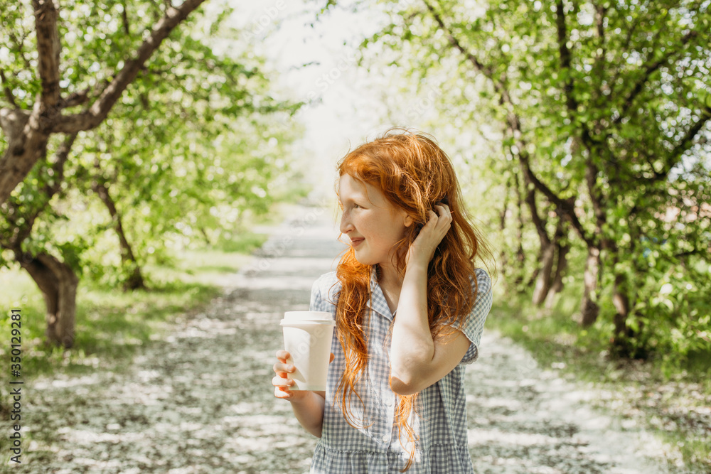 Red-haired little girl drinks tea in a glass on a walk Red-haired little girl drinks tea in a glass on a walk